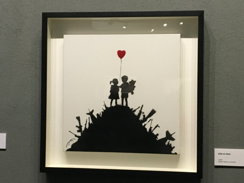 girl and boy holding a heart shaped balloon on a pile of guns