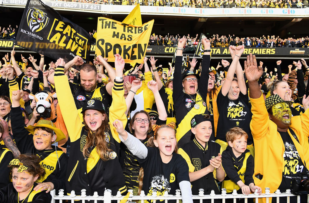 young and old richmond supporters waving flags and banners at a football game