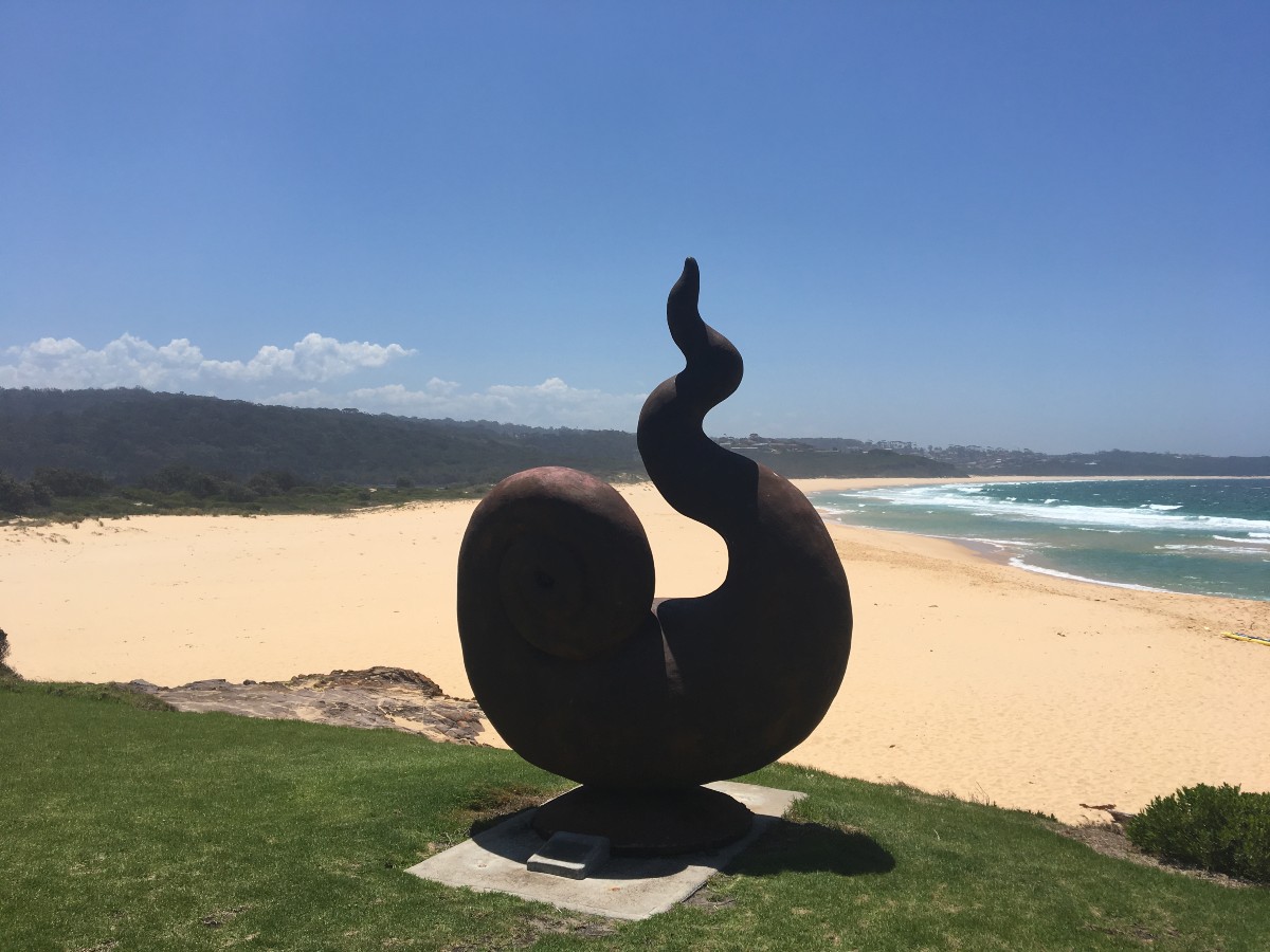 shell like steel or metal sculpture with a view of the beach in the distance - merimbula nsw