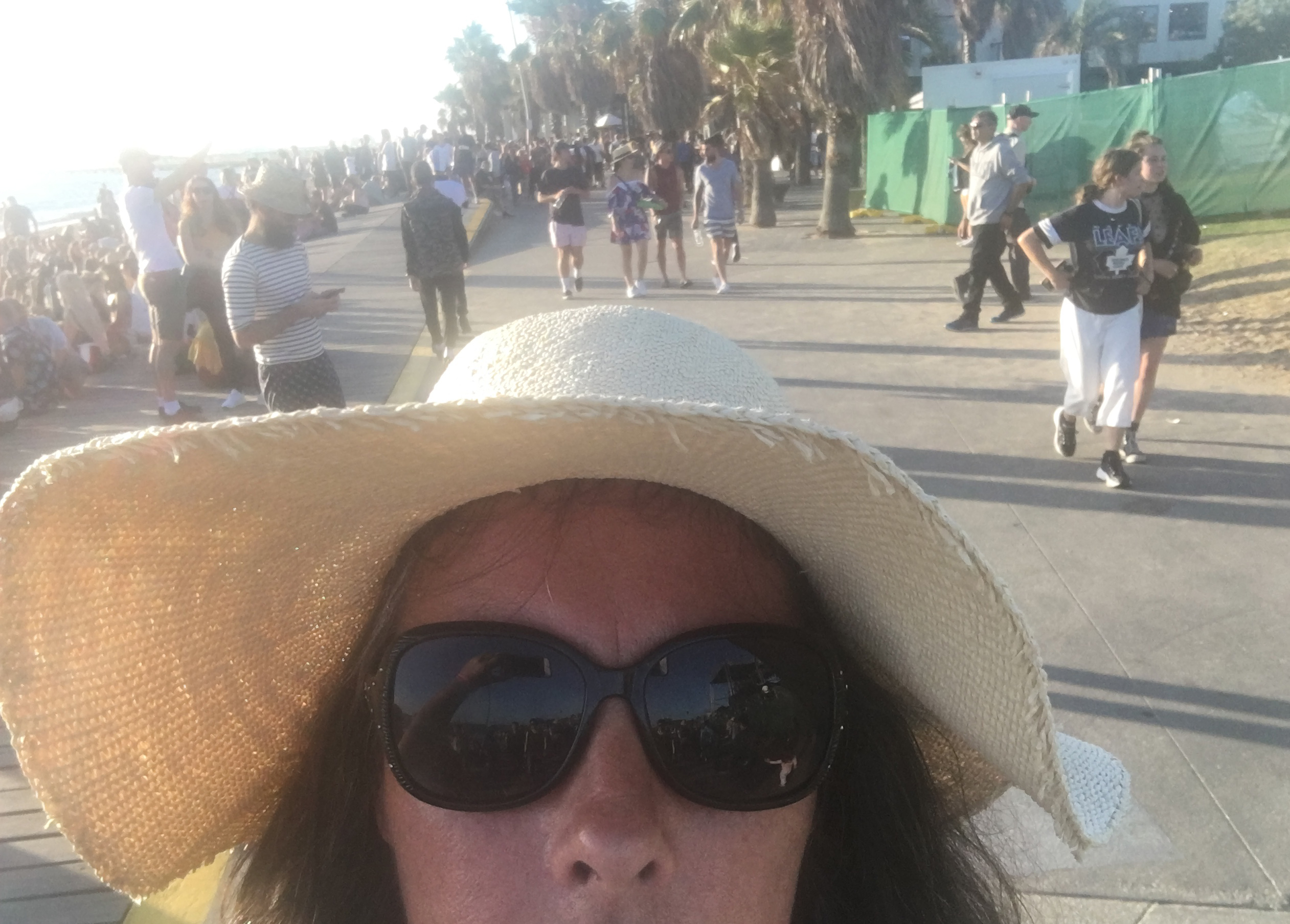 people beyond on a boardwalk at the beach at st kilda festival with pipeldoot in the front in a hat and sunglasses
