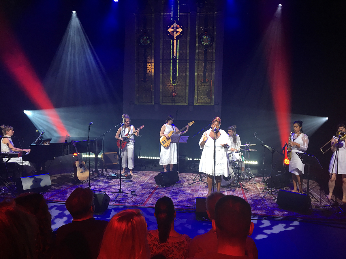 stage bathed in blue and red light filled with women wearing white and playing music - for thando summer sessions
