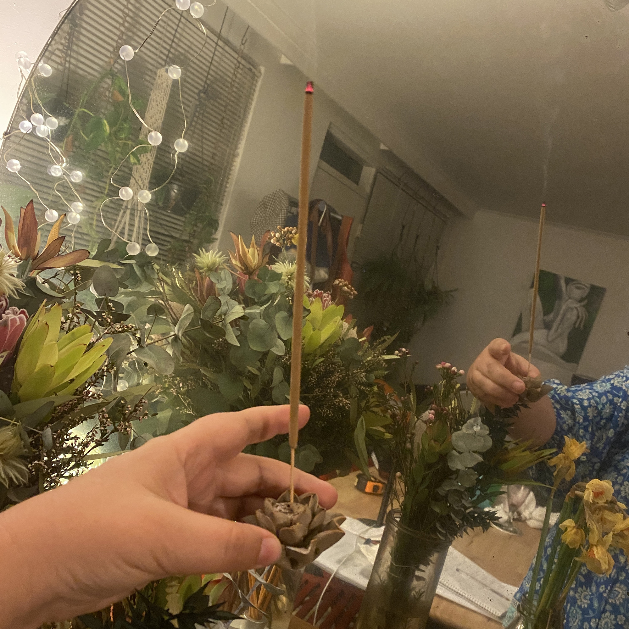sarah holding incense in front of a mirror and lots of bunches of flowers - you can see the incense smoke in the mirror