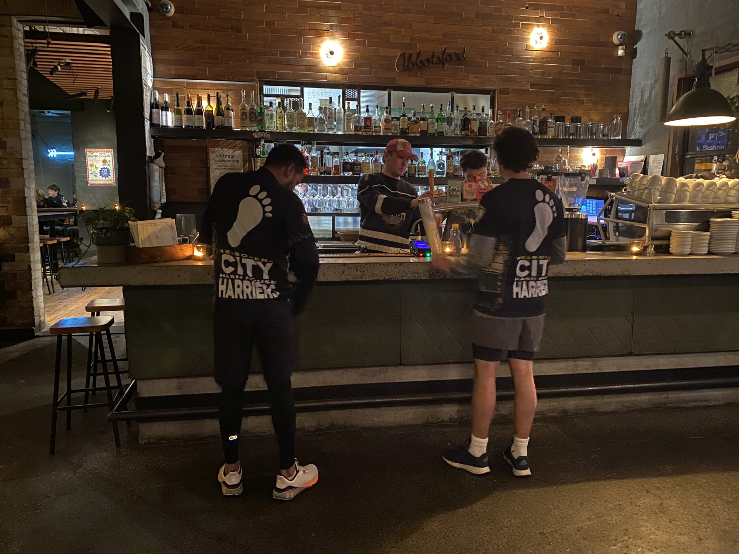 two men with city harriers t-shirts on stand in front of a bar in Abbotsford